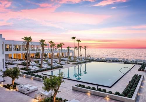 Main pool area with views of the sea and sunset at the Grecotel LUX ME White Palace in Crete, Greece.